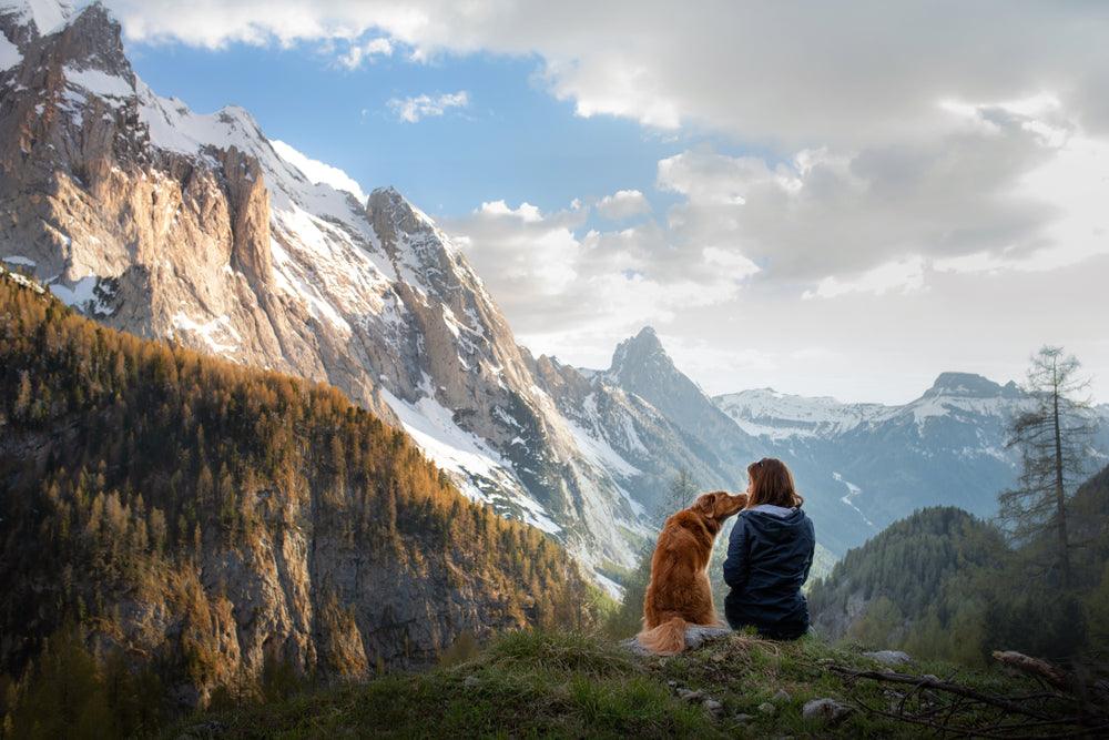 woman and dog sitting in in front of a mountain